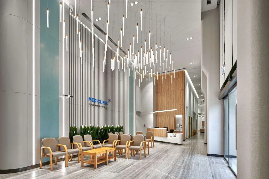 Modern medical clinic reception with soft seating, vertical acoustic panels, indoor greenery, and sculptural pendant lighting at Mediclinic Dubai Creek Harbour.