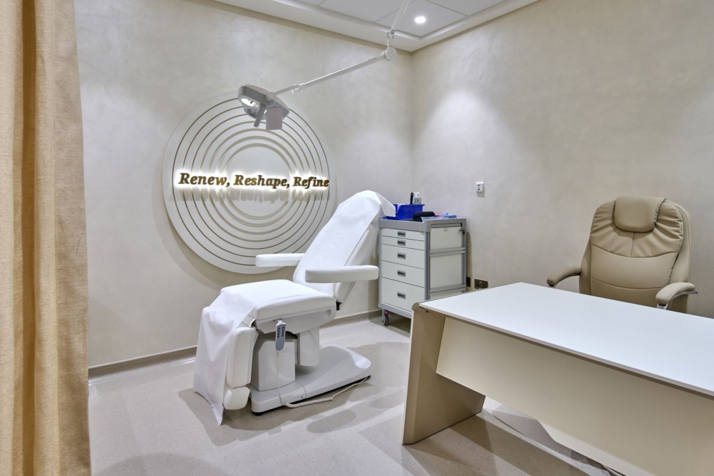 Modern dermatology treatment room with ergonomic chair, medical lighting, neutral tones, and a sign reading 'Renew, Reshape, Refine'.