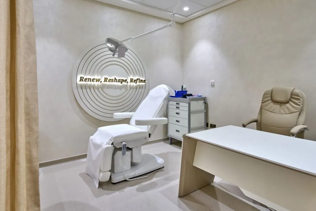Modern dermatology treatment room with ergonomic chair, medical lighting, neutral tones, and a sign reading 'Renew, Reshape, Refine'.