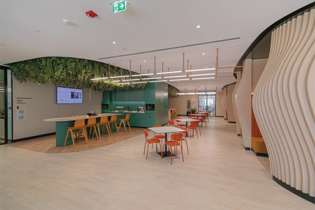 Modern office pantry with biophilic ceiling, green cabinetry, wave-like timber slat feature wall, and flexible dining layout designed by Summertown Interiors