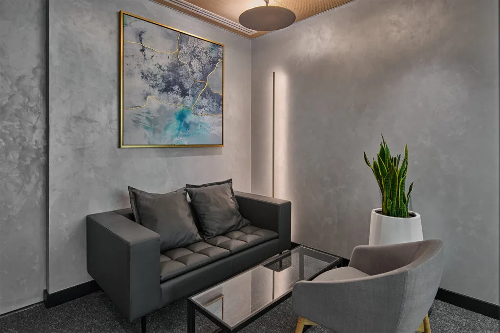 Modern waiting area featuring a black sofa, grey armchair, glass coffee table, abstract artwork, and a snake plant in a white pot – designed by Summertown Interiors for Global Capital Management in DIFC Gate Building 5