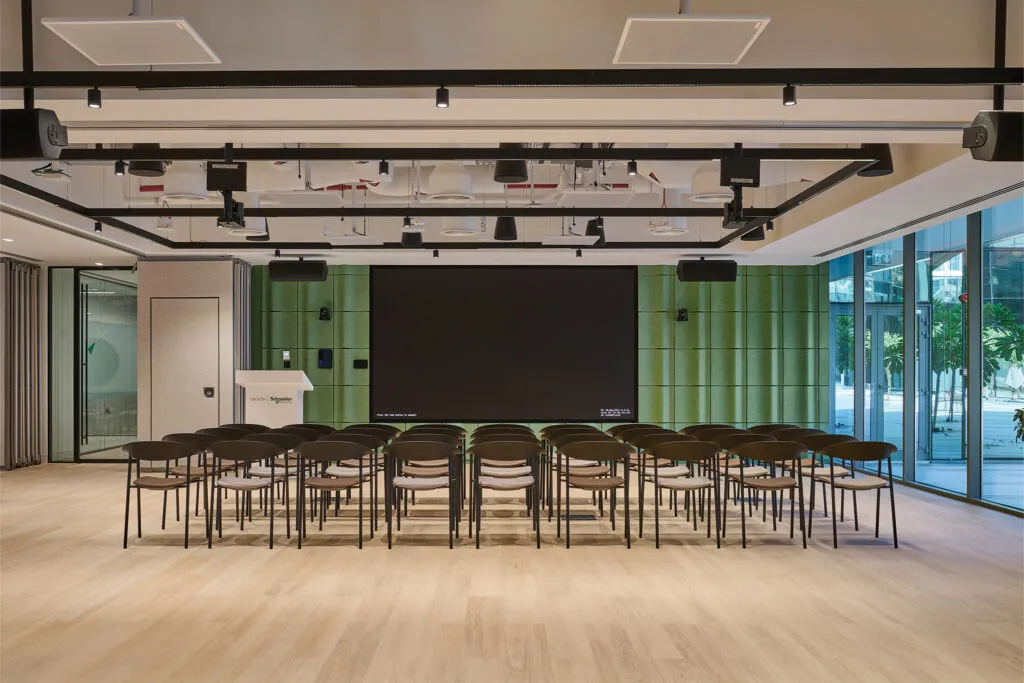 Sustainable office fit-out in Dubai featuring the Schneider Electric Innovation Hub auditorium with green acoustic wall panels, modern seating, and large presentation screen