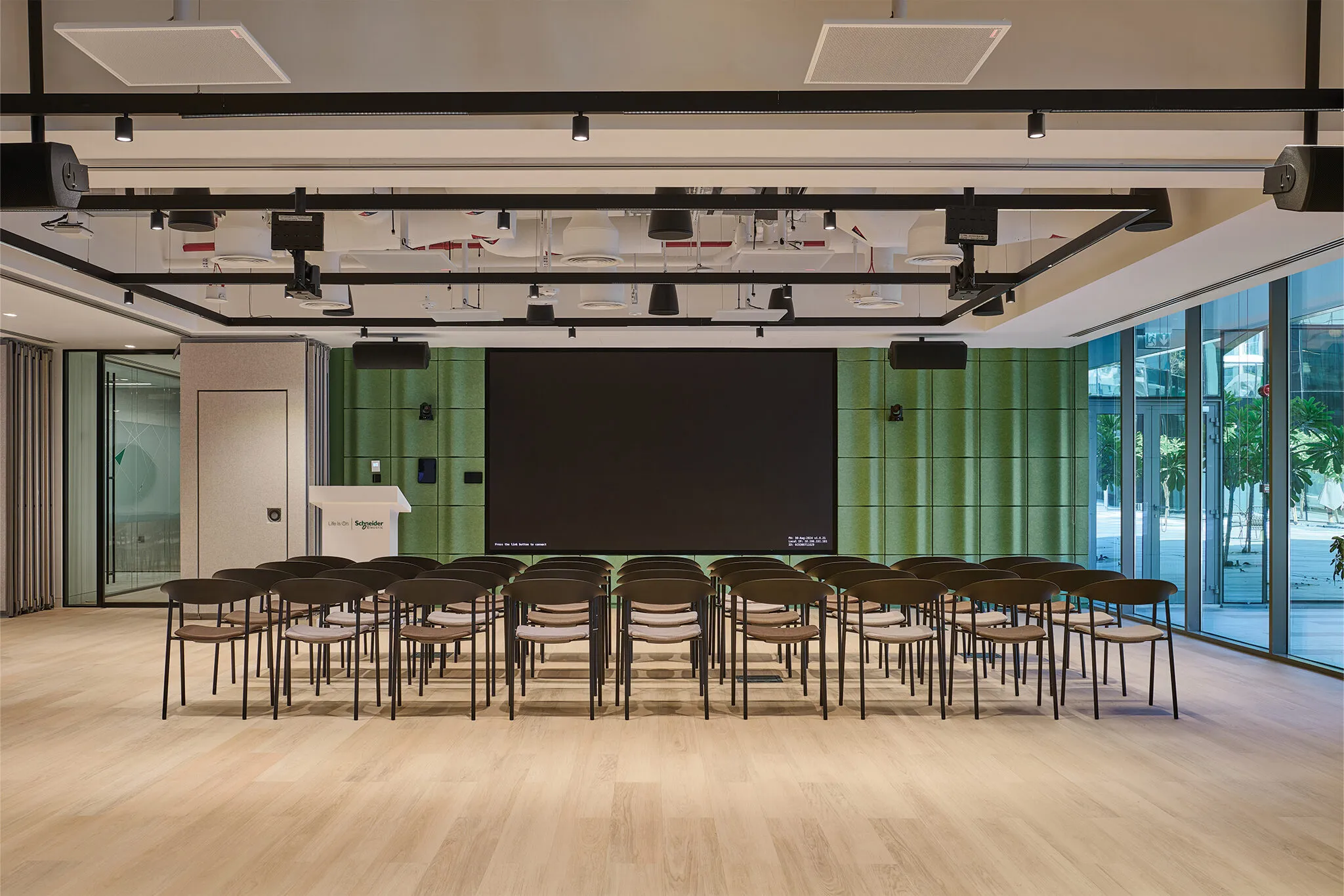 Sustainable office fit-out in Dubai featuring the Schneider Electric Innovation Hub auditorium with green acoustic wall panels, modern seating, and large presentation screen