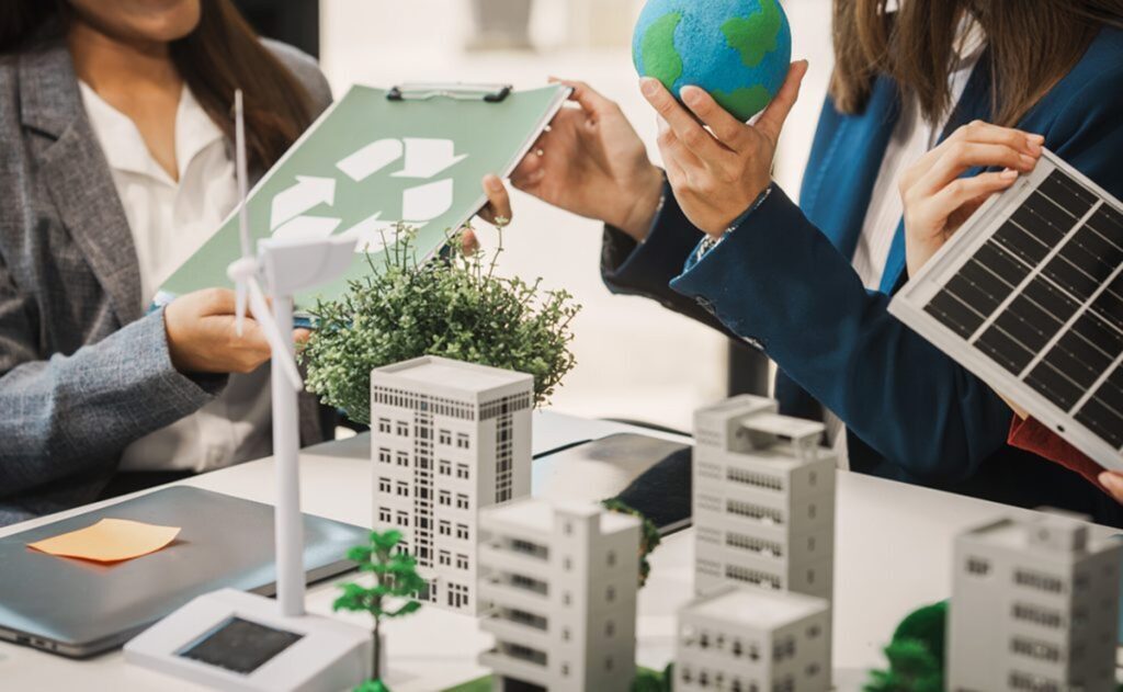 Business professionals discussing sustainable office design, holding a globe, solar panel, and recycling chart.