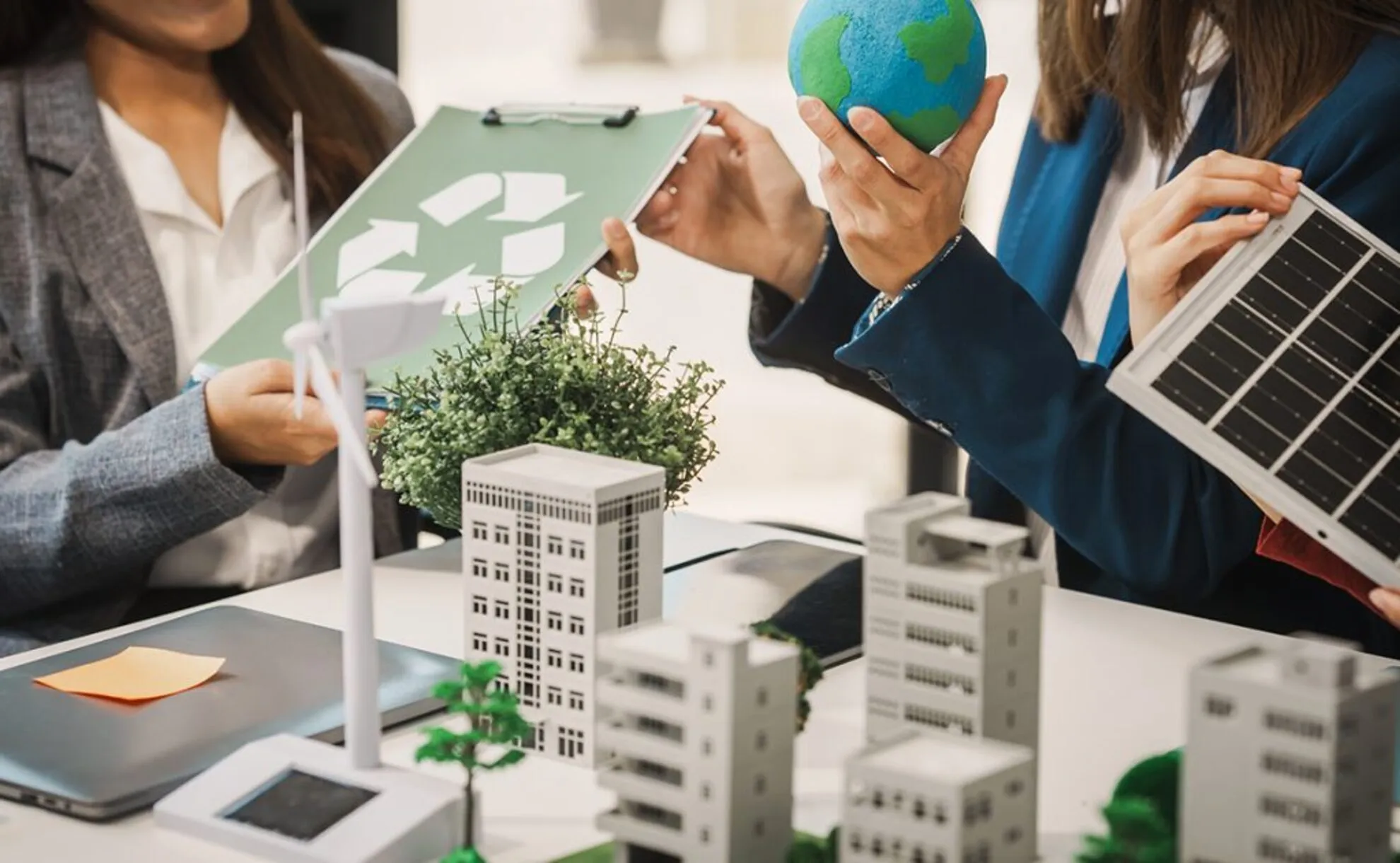 Business professionals discussing sustainable office design, holding a globe, solar panel, and recycling chart.